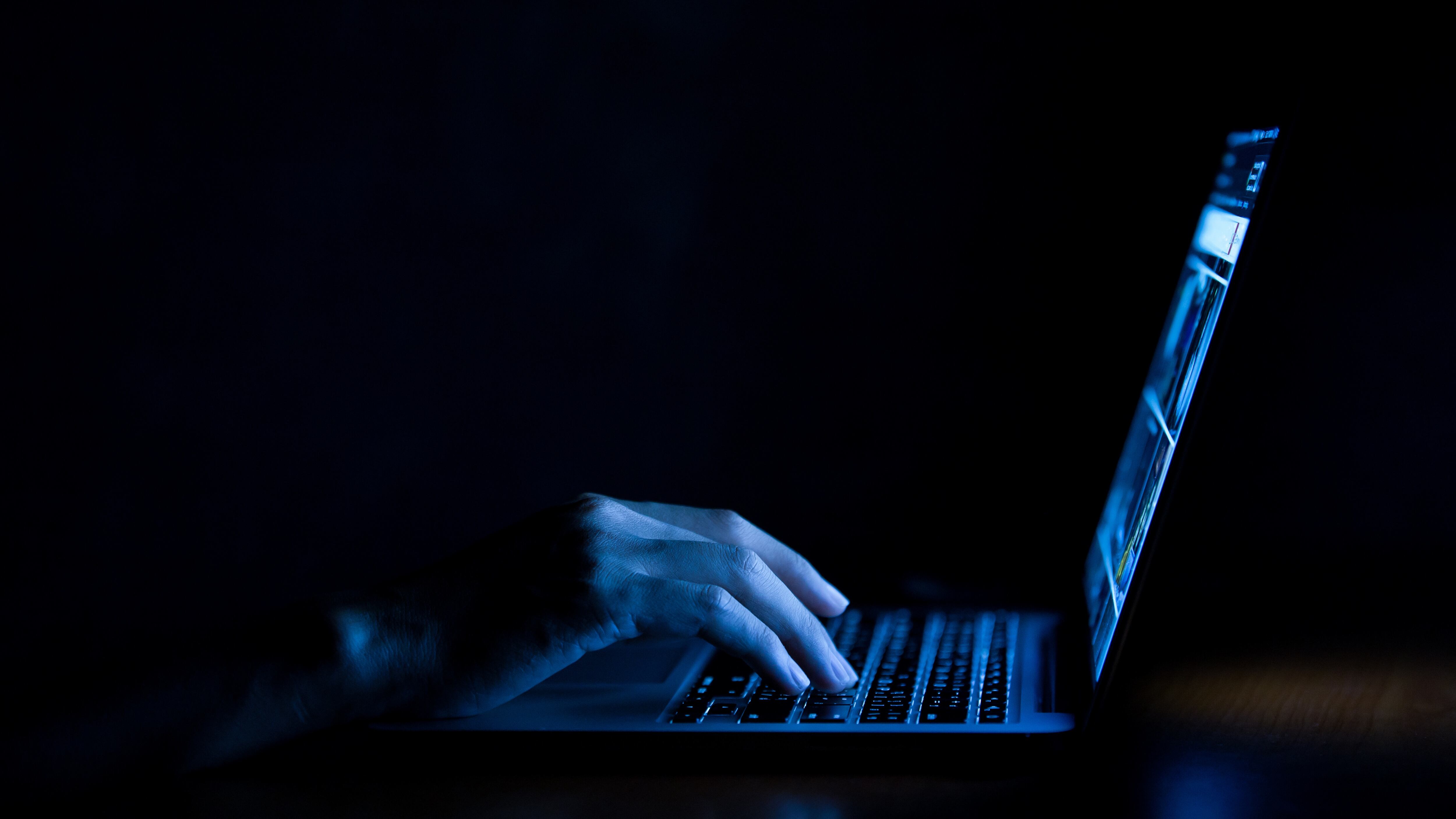 Hand of a man using laptop computer for hacking or steal data at night in office. Hacking concept